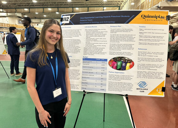Student posing next to her presentation poster