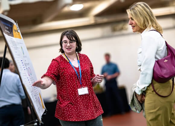 A student pointing to a poster presenting her project to a woman
