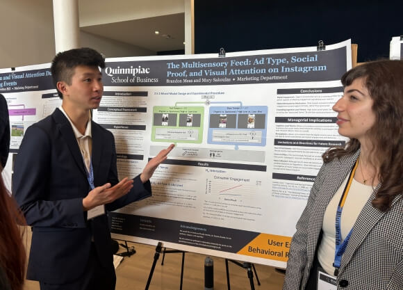Photo of Brandon Meas and Mary Sakoulas standing in front of poster