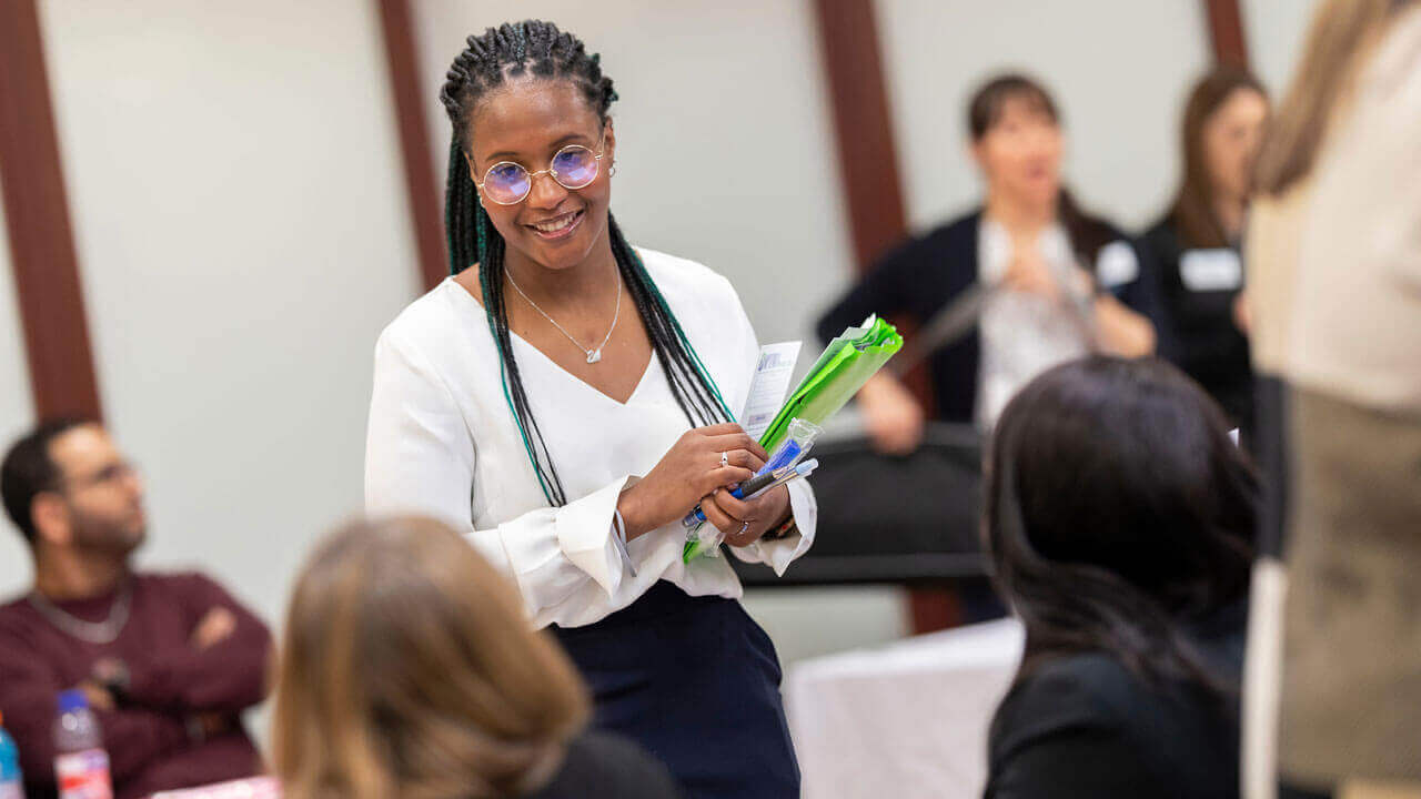 A student standing and smiling with a folder in hand.